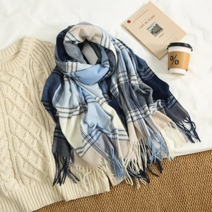 Detail of plaid tassel scarf in navy and khaki laid on a cable knit sweater