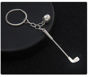 Detail of silver golf club and ball keychain pendant on a professional black base