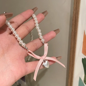 Close-up of pink velvet bow and silver heart pendant on a white pearl necklace