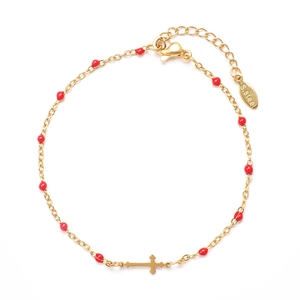 Detail of golden stainless steel bracelet with red beads and a cross pendant charm