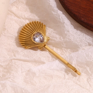 Close-up of a gold scallop hair clip with a teardrop crystal on textured white paper