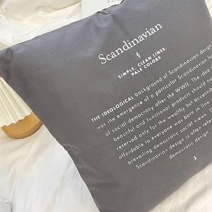 Dettaglio copricuscino grigio scuro con scritte scandinave su un letto bianco minimalista