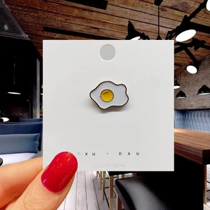 Macro detail of cartoon fried egg enamel pin brooch on a jewelry display card