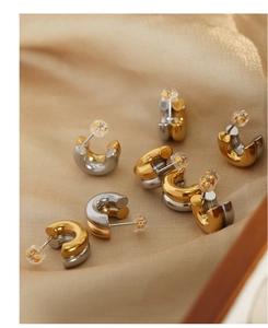Detailed macro of two-tone gold and silver C-shape earrings on elegant champagne silk fabric
