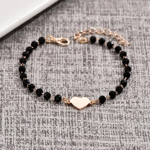 Minimalist beaded cross bracelet with a rose gold heart pendant on textured background