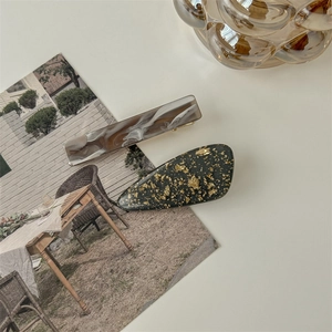 Detail of amber marble resin and gold foil black droplet hair clips on a desk