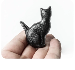 Detailed macro view of a black cast iron cat-shaped drawer handle held in hand