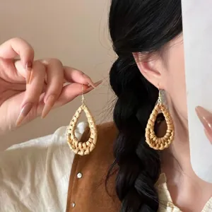 Detail of hand-woven teardrop rattan earrings with golden hooks on female model