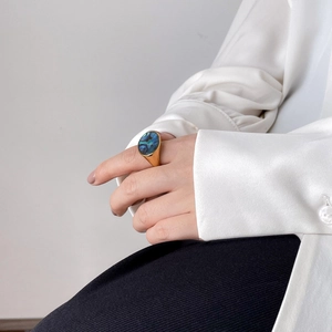 Close-up of a gold signet ring with iridescent shell inlay worn by a model