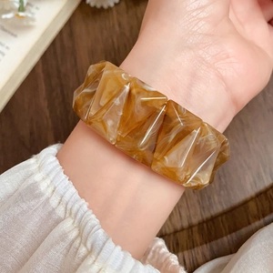 Detailed view of an amber acrylic faceted geometric bracelet on a model's wrist