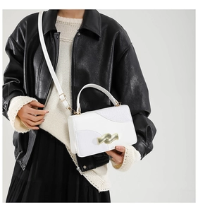 Detail of white textured leather handbag featuring a wavy gold clasp and animal embossed flap