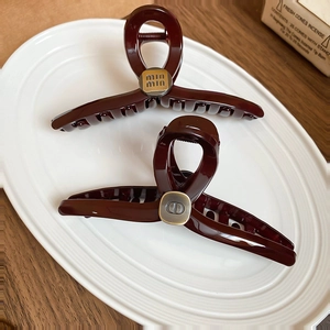 Close-up of deep wine red acrylic hair claws with gold and silver metal logo plaques