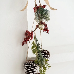 Christmas hanging decoration with pine cones, red berries, and golden bell on white wall