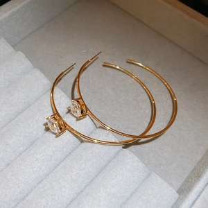 Détail macro de boucles d'oreilles en C dorées avec zircon rond sur support en velours