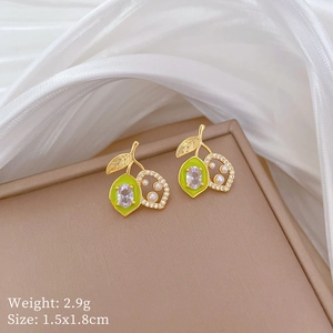 Macro shot of gold lemon earrings with green enamel and white pearls on silk