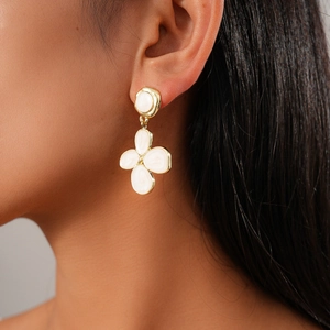 Macro view of gold flower earrings with white enamel finish on a female model