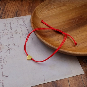Close-up of red braided rope bracelet with a gold 3D heart pendant on vintage paper