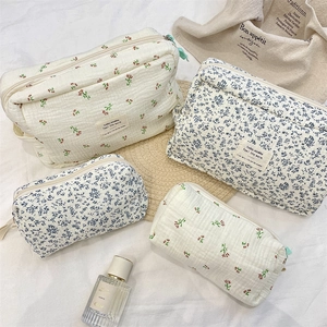 Quilted cotton toiletry bags with floral patterns on white bedding in lifestyle setting