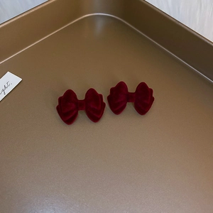 Close-up of a pair of deep red velvet bow earrings with pearls in a gold tray
