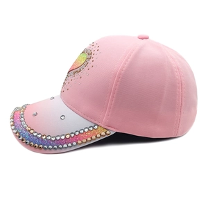 Detail of pink baseball cap featuring sequin heart design and gradient rhinestone brim