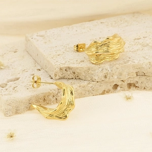 Textured gold C-shaped earrings with irregular ripple design on beige stone