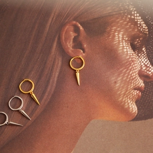 Detailed view of silver and gold conical hoop earrings displayed over a fashion portrait