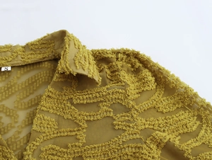 Detail of V-neck collar showing size S tag and textured fringe fabric on green blouse