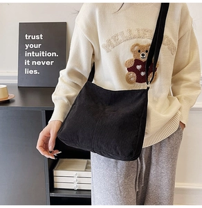 Detail view of a black corduroy crossbody bag worn by a model in a casual indoor setting