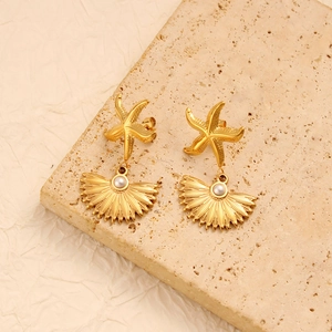 Detail view of gold starfish and shell earrings with a white pearl on a natural stone