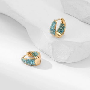 Macro shot of geometric gold earrings with pavé set blue zircon on textured white stone