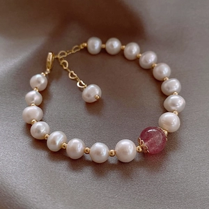 Detail of strawberry quartz bead and white pearls on a gold link bracelet closure