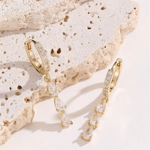 Elegant gold drop earrings with sparkling cubic zirconia on a minimalist stone background