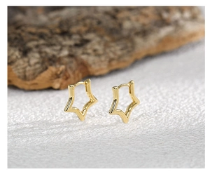 Macro shot of polished gold star-shaped huggie earrings on minimalist stone texture