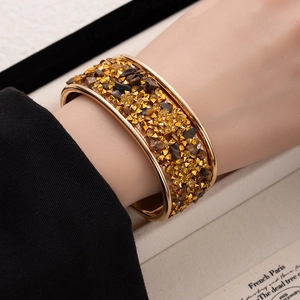 Detailed view of gold wide open bangle with pave crystals and tiger eye stones