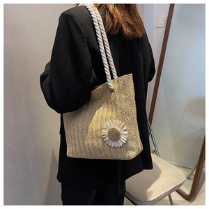 Detail of hand-woven straw tote bag with white daisy flower and cotton rope handle