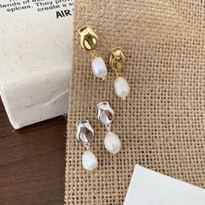 Detail of irregular freshwater pearl drop earrings in gold and silver finishes on a rustic base