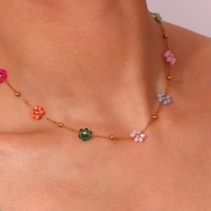 Close-up of a delicate gold chain necklace with colorful beaded flower charms on neck