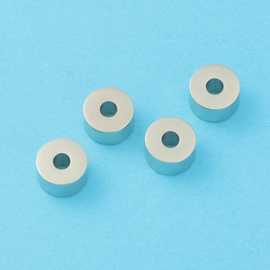 Macro shot of four polished cylindrical metal beads for DIY jewelry on a blue background