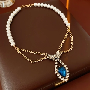 Detail of vintage necklace featuring blue teardrop pendant, pearl chain, and rhinestone bow