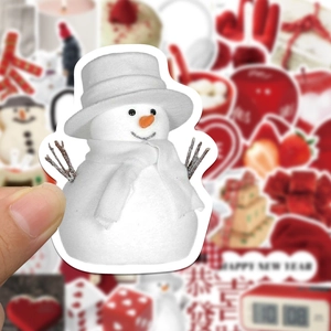 Close-up of hand holding a cute white snowman sticker with festive holiday background
