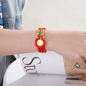 Detail of layered red glass bead bracelet with gold coin charm on person