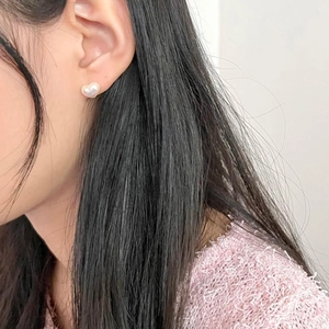 Close-up of a model wearing minimalist heart-shaped pearl stud earrings in warm white