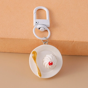 Detailed view of realistic resin cake charm with golden spoon on a white plate keychain