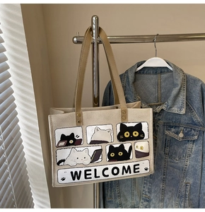 Detail of beige canvas tote bag showing cat print and welcome text in natural light
