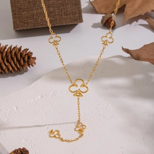 Collana lunga a Y dorata con ciondolo a fiori e nappa su sfondo naturale di pigne e foglie