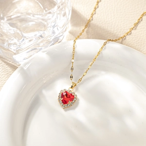 Elegant gold heart necklace with red gemstone and white zircons on white ceramic plate