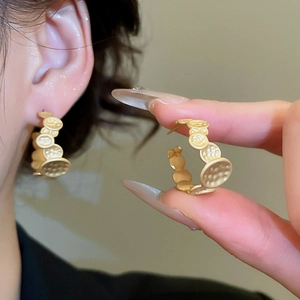 Macro detail of matte gold C-shaped hoop earrings with textured hammered metal finish