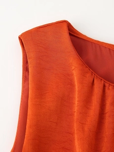 Detail of orange sleeveless dress showing textured satin fabric and pleated neckline finish