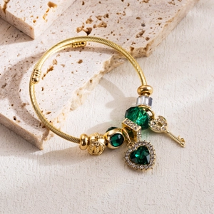 Macro shot of gold spiral bangle with green heart gemstone and crown charms on stone