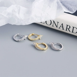 Detail of silver and gold flower earrings with pavé zircons on a blue backdrop